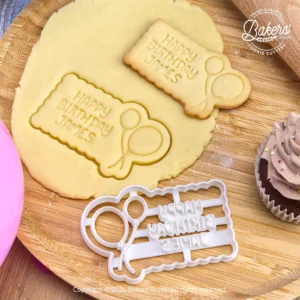 Emporte-pièce biscuit Happy Birthday personnalisé avec prénom et ballons. Photo montrant la découpe dans la pâte sablée et le biscuit d’anniversaire fini. Idéal pour réaliser facilement des biscuits anniversaire maison.