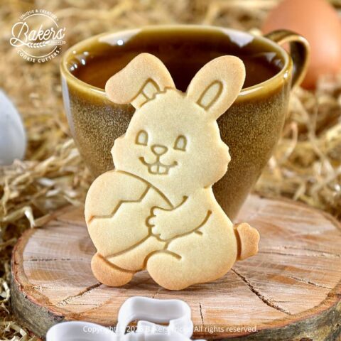 Biscuit lapin de Pâques tenant un œuf réalisé avec un emporte-pièce Bakers'Tricks, biscuit sablé doré photographié devant une tasse