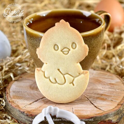 Biscuit poussin de Pâques réalisé avec un emporte-pièce Bakers'Tricks, biscuit sablé doré posé devant une tasse dans une ambiance rustique