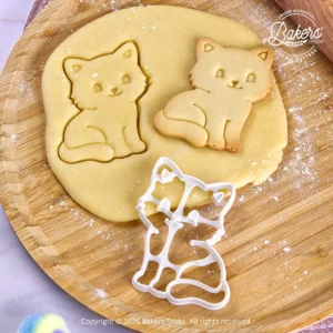 Emporte-pièce Chat assis Bakers'Tricks découpant une pâte sablée avec le biscuit réalisé juste à côté.
