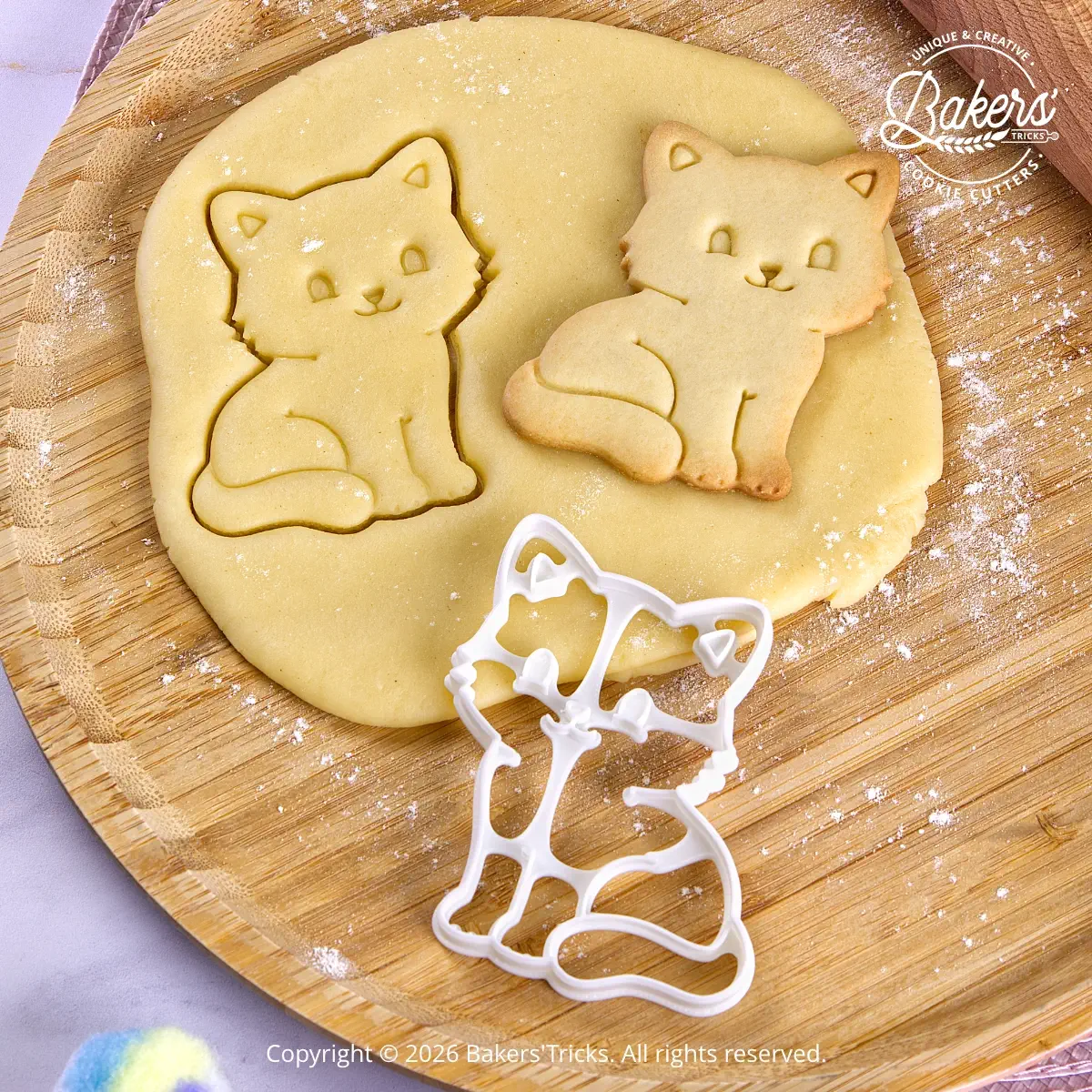 Emporte-pièce Chat assis Bakers'Tricks découpant une pâte sablée avec le biscuit réalisé juste à côté.