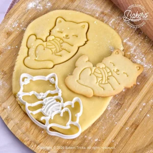 Emporte-pièce Chat avec sa pelote de laine Bakers'Tricks découpant une pâte sablée avec le biscuit réalisé juste à côté.